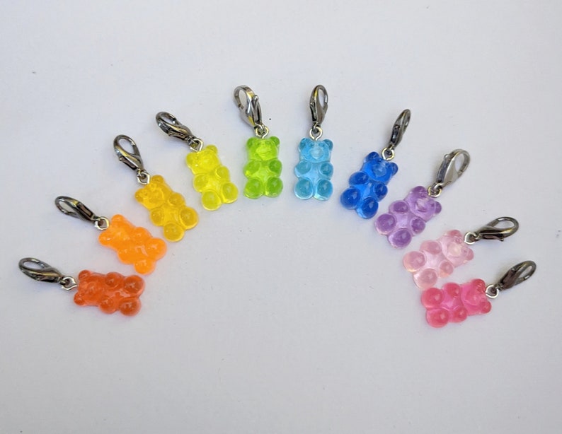 Puede incluir: Diez abalorios con forma de osito de goma de colores con cierres plateados. Los abalorios est&aacute;n dispuestos en forma de arco&iacute;ris, comenzando por el naranja y terminando por el rosa.
