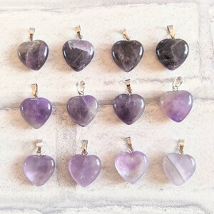 May include: Twelve amethyst heart-shaped pendants with silver bail. The pendants are arranged in three rows of four.