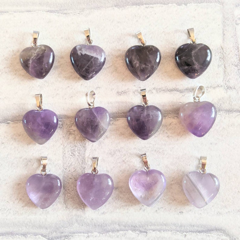 May include: Twelve amethyst heart-shaped pendants with silver bail. The pendants are arranged in three rows of four.
