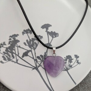 May include: A purple heart-shaped amethyst pendant on a black cord necklace.