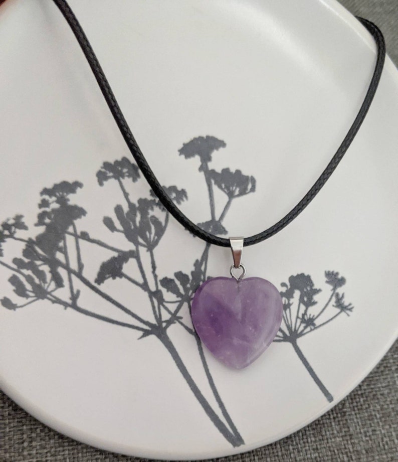May include: A purple heart-shaped amethyst pendant on a black cord necklace.