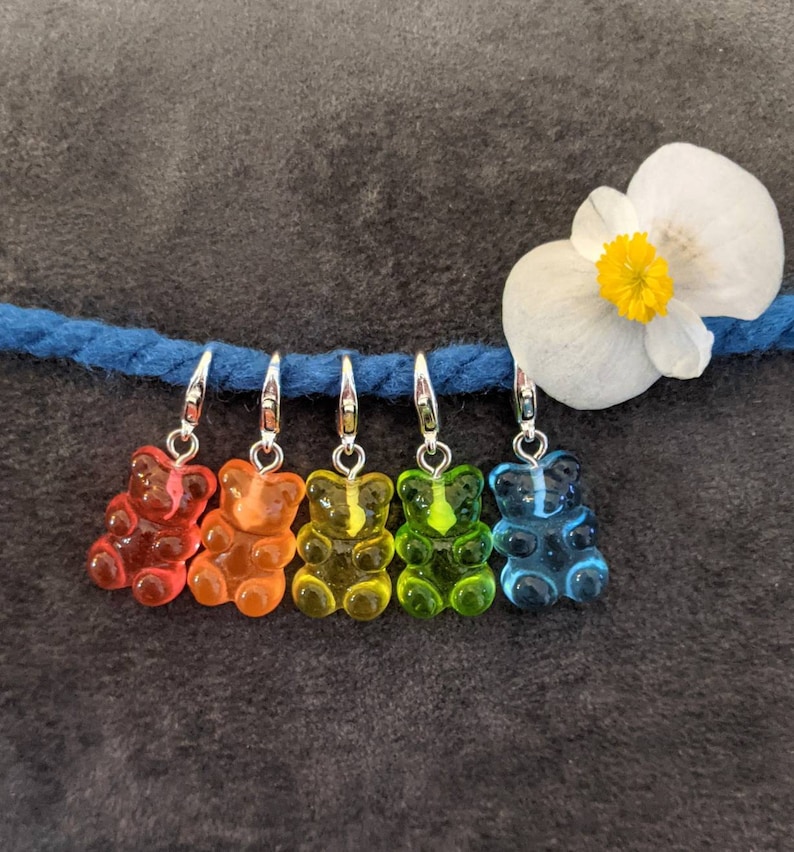 Puede incluir: Cinco marcadores de punto en forma de osito de goma en un arco&iacute;ris de colores: rojo, naranja, amarillo, verde y azul. Los marcadores est&aacute;n unidos a un hilo azul con anillos plateados.