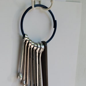 May include: A set of wrenches hanging on a blue ring, with a larger wrench hanging below. The wrenches are silver and the larger wrench is black.