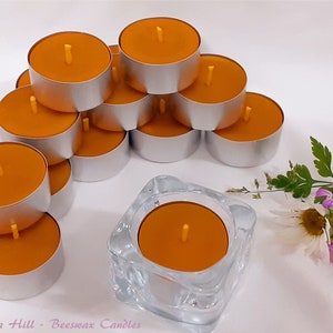 May include: A stack of 12 orange beeswax tea light candles in silver holders. The candles are arranged in a pyramid shape. There is a single orange beeswax candle in a clear glass holder in the foreground. The text "Light on a Hill - Beeswax Candles" is visible at the bottom of the image.