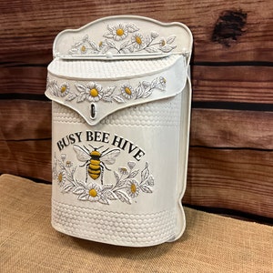 May include: White metal mailbox with a bee and flower design. The mailbox has the text "Busy Bee Hive" on the front.