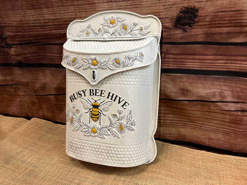 May include: White metal mailbox with a bee and flower design. The mailbox has the text "Busy Bee Hive" on the front.