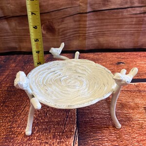May include: White cast iron bird bath with a textured, circular bowl. The bowl is supported by three legs and adorned with bird figurines. The bird bath measures approximately 7 inches in height.