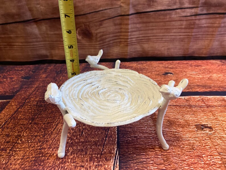 May include: White cast iron bird bath with a textured, circular bowl. The bowl is supported by three legs and adorned with bird figurines. The bird bath measures approximately 7 inches in height.