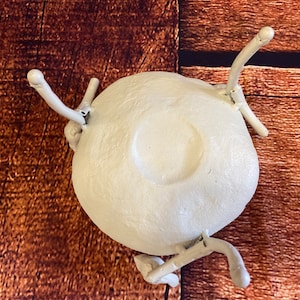 May include: A white, round, ceramic object with four curved, white, arm-like extensions. The object has a central, recessed circular area. The background is a brown, wooden surface.