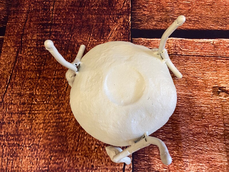 May include: A white, round, ceramic object with four curved, white, arm-like extensions. The object has a central, recessed circular area. The background is a brown, wooden surface.