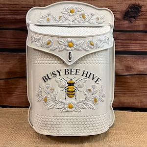 May include: White metal mailbox with a bee and flower design. The mailbox has the text "Busy Bee Hive" on the front.