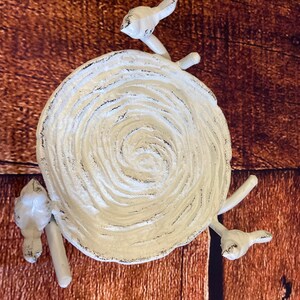 May include: A white, cast iron decorative plate with a spiral design. The plate is adorned with three bird figures, each perched on a branch extending from the plate's edge. The plate has a distressed finish with black accents, set against a wooden background.