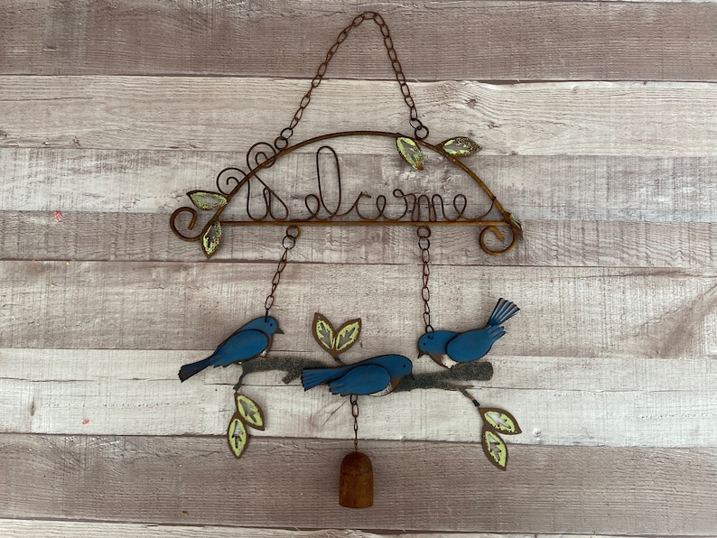 May include: A metal welcome sign with blue birds and leaves hanging from it. The sign is rusty and has a rustic look.
