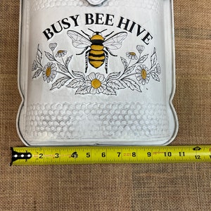 May include: White metal mailbox with a black and yellow bee and flowers. The mailbox has the words "Busy Bee Hive" printed on it. The mailbox is 10 inches wide.