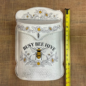 May include: White metal mailbox with a bee and flower design. The mailbox has the text "Busy Bee Hive" on the front.