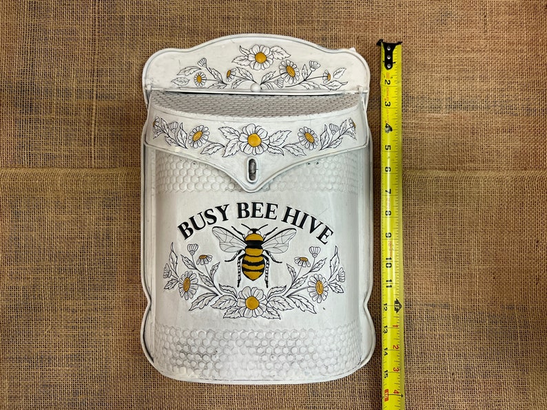 May include: White metal mailbox with a bee and flower design. The mailbox has the text "Busy Bee Hive" on the front.