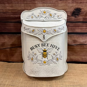 May include: White metal mailbox with a bee and flower design. The mailbox has the text "Busy Bee Hive" on the front.
