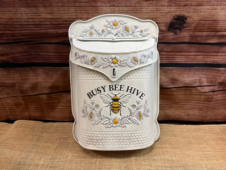 May include: White metal mailbox with a bee and flower design. The mailbox has the text "Busy Bee Hive" on the front.