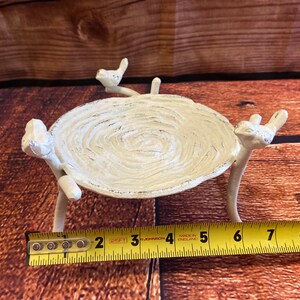 May include: A white, bird-themed decorative tray. The tray is oval-shaped, with a textured surface and supported by three bird-shaped legs. The tray is approximately 6 inches long.