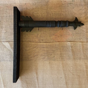 May include: Black wooden arrow sign with a pointed tip and a flat back. The sign is mounted on a black wooden base.