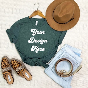 May include: A green t-shirt with the text "Your Design Here" in white. The t-shirt is on a white surface with a brown hat, blue jeans, and leopard print shoes.