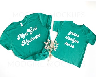 May include: Two teal green t-shirts, one adult size and one child size, with white text. The adult shirt says "Mod Girl Mockups" and the child shirt says "your design here".