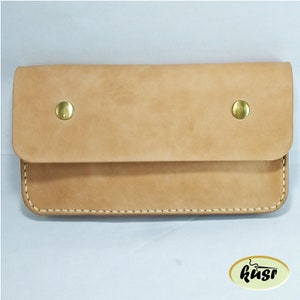 May include: A light tan leather wallet with a flap closure secured by two brass snap buttons. The edges are stitched with a light-colored thread. The wallet has a rectangular shape and a minimalist design.
