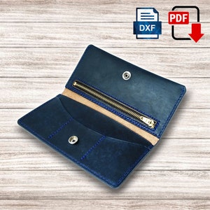 May include: Open navy blue leather wallet with a zipper closure and snap button. The interior features card slots and a light tan lining. Blue stitching accents the edges. The wallet is shown open, displaying its compartments.