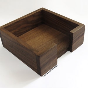 K&ouml;nnte beinhalten: Ein quadratischer Holz-Tischtuchhalter aus dunklem Walnussholz. Die Box hat eine einzelne &Ouml;ffnung an einer Seite f&uuml;r einfachen Zugang zu den Taschent&uuml;chern.
