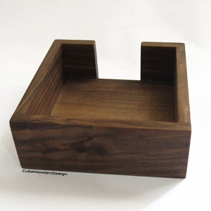 K&ouml;nnte beinhalten: Ein dunkelbrauner, quadratischer Holz-Tischtuchhalter mit offener Oberseite. Der Halter ist aus massivem Holz gefertigt und hat eine nat&uuml;rliche Oberfl&auml;che. Der Text "CubeWoodenDesign" ist auf der Unterseite des Halters sichtbar.