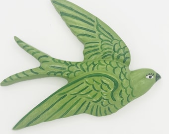 May include: A wall-mounted swallow bird ornament crafted in a light green hue with darker green painted feather details. The bird is depicted in a flying position with wings extended and a forked tail, featuring a small eye with painted eyelashes.