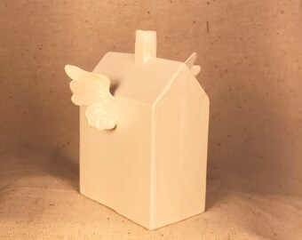 May include: White ceramic house figurine with a single wing extending from the side. The house has a simple design with a chimney on the roof.