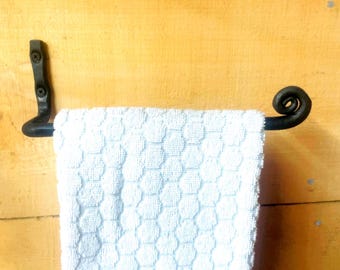 May include: A black metal towel bar with a curled end and a flat mounting bracket featuring two visible screws. A white hand towel with a raised, repeating hexagonal texture is draped over the bar, hanging vertically from the horizontal metal rod.