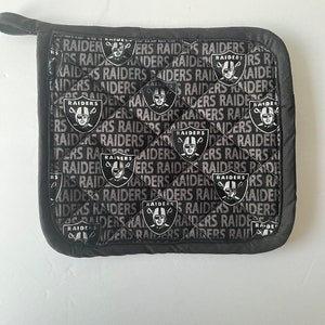 Pode incluir: Manopla de forno acolchoada em preto e branco com o logotipo dos Las Vegas Raiders e a palavra "Raiders" repetida por toda parte.