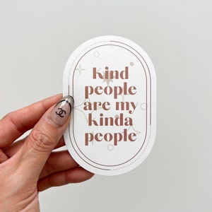 Puede incluir: Pegatina ovalada blanca con un contorno marrón y un texto que dice "Kind people are my kinda people". La pegatina tiene un diseño de estrella y círculo marrón.