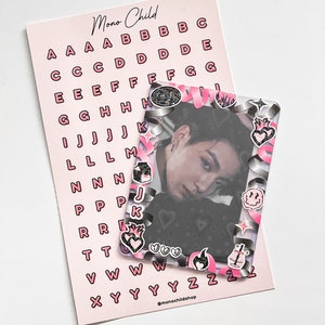 May include: A pink sheet of alphabet stickers and a photo card. The stickers are pink with black outlines. The photo card has a decorative frame with pink and silver accents and various stickers. The text "Mono Child" is visible.