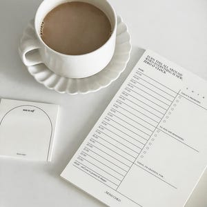 May include: A white planner with a black and white design. The planner has a daily schedule, a to-do list, and a gratitude section. The text on the planner reads "Turn this all around when everything is new, Zero O' Clock".