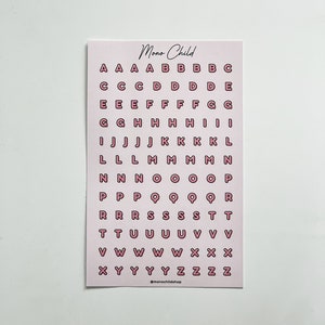 May include: A pink card with the text "Mono Child" at the top and a grid of pink letter stickers. The letters are outlined in a darker pink. The bottom of the card has the text "@monochildshop".