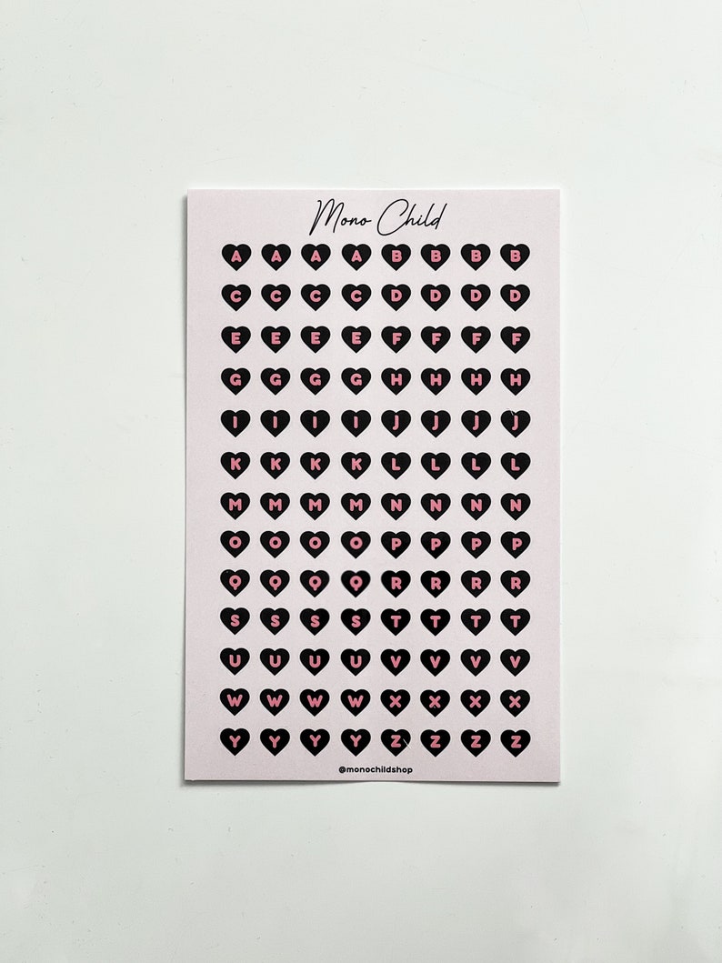 May include: A sheet of pink stickers with black heart shapes, each containing a letter of the alphabet in pink. The text "Mono Child" is at the top, and "@monochildshop" is at the bottom.