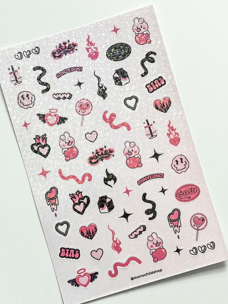 May include: Sheet of stickers with a glittery background. The stickers feature pink and black designs, including hearts, flames, a bunny, and text that reads "BIAS", "ANNYEONG!", and "MAKNAE". The stickers are in various shapes and sizes.