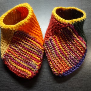 May include: A pair of colorful knitted slippers with a yellow, orange, red, purple, and brown striped pattern. The slippers have a yellow cuff.