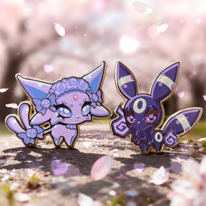 Puede incluir: Dos pines de esmalte con criaturas de dibujos animados estilizadas. Uno es lavanda con una corona floral, el otro es morado oscuro con detalles dorados. Ambos tienen ojos grandes y están sobre un fondo floral rosa borroso.