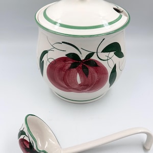 May include: A white ceramic soup tureen with a matching lid and a long-handled ladle. The set features hand-painted red tomatoes with green leaves and vines, accented by thin green trim along the edges of the lid, the bowl, and the ladle.
