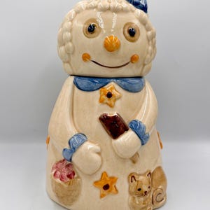 May include: A ceramic cookie jar in the shape of a smiling doll with a blue bow, blue accents, and star details. The doll holds a chocolate ice cream bar and has a basket of treats and a squirrel on the base.
