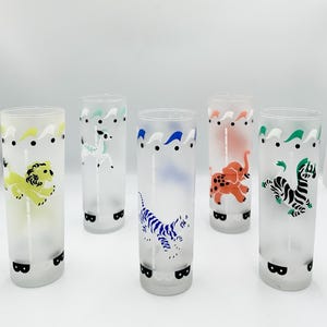 May include: Set of five frosted glass tumblers with animal designs. Each glass features a different animal: a yellow lion, a white deer, a blue tiger, an orange elephant, and a black and white zebra. The glasses have a decorative wavy border.