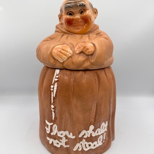 May include: A vintage ceramic cookie jar shaped like a smiling monk in a brown robe. The jar has a removable lid and the words "Thou shalt not steal!" are written on the front in white script.