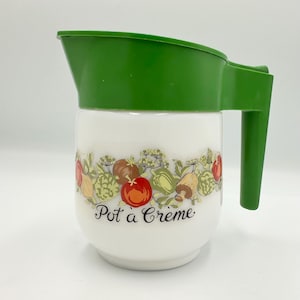 May include: White ceramic "Pot à Crème" container with a green plastic lid and handle. The container is decorated with a colorful illustration of vegetables and the text "Pot à Crème".
