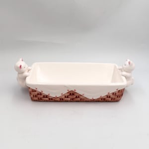 May include: A rectangular ceramic serving dish with a basket weave design. The dish has a white interior and is trimmed with a brown basket weave pattern. Two white cat figurines are on each end of the dish. The dish is approximately 10 inches long.