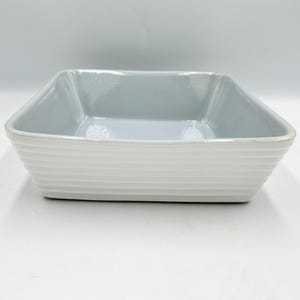 May include: A white ceramic mug with a black handle and the text "But First, Coffee" in a black, bold font. The mug is sitting on a white surface. The mug appears to be empty.