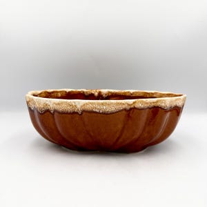 May include: A brown ceramic planter with a scalloped design. The planter has a glossy finish and a light brown, textured rim. The interior is a darker brown. This vintage piece is suitable for indoor or outdoor use.